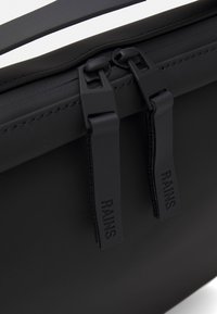 Schwarze wasserdichte Tasche mit zwei schwarzen Reißverschlüssen, auf denen "RAINS" eingeprägt ist, glatter, matter Textur und minimalistischem Design.