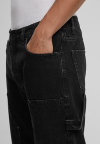 Sort denim cargo bukser med lige pasform, sidelommer og baglommer samt kontrasterende syninger. Materialet er robust og struktureret.