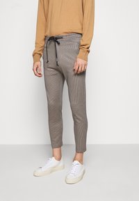 Szare w kratkę tapered spodnie z elastycznym pasem, z regulowanym sznurkiem oraz bocznymi kieszeniami, w połączeniu z białymi trampkami.