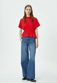 Top corto rosso a maniche corte con vita arricciata e orlo arricciato, abbinato a jeans in denim blu a gamba larga e scarpe nere. Design minimalista.