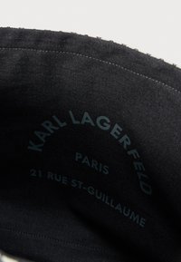 Fekete textil belső, amelyen nyomtatott szöveg található: "KARL LAGERFELD PARIS 21 RUE ST-GUILLAUME." Egyszerű varrás a szélein.