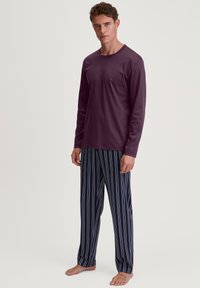Maglia a maniche lunghe viola abbinata a pantaloni da pigiama a righe blu navy con strisce rosse e bianche, realizzata in un tessuto morbido con una texture liscia.