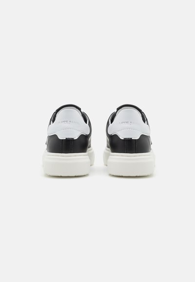 Baskets noir et blanc avec une tige en cuir lisse, des panneaux texturés contrastants, des semelles blanches épaisses et un logo en relief au niveau du talon.