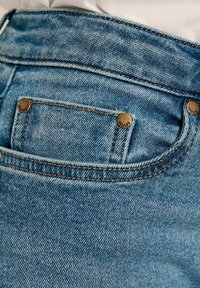 Jeans de mezclilla azul claro con herrajes de cobre, costuras de contraste y un pequeño bolsillo trasero con botones de marca.