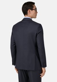 Jūras spēku zila pinstripe uzvalka žakete ar strukturētu piegriezumu, izgrieztiem klājiem, vienu spraugu un pogājamām aprocēm. Aizmugures skats parāda pielāgotu siluetu.