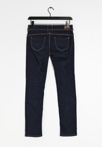 Mörkblå denim skinny jeans hängande på en svart galge. Har två bakfickor med dekorativ sömnad och synliga sömmar.