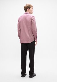 Camicia a maniche lunghe con colletto di un leggero color marrone, presenta un motivo sottile, polsini abbottonati, abbinata a pantaloni neri a gamba tapered e scarpe.