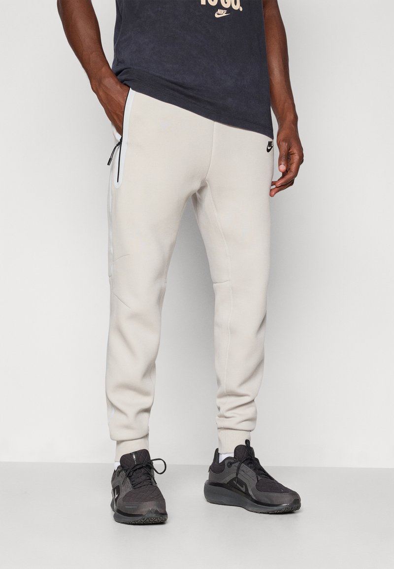 Ljusbeige sweatpants med avsmalnande passform, elastiska muddar och dragkedjeförsedda sidofickor. Kombinerade med mörka sneakers med en strukturerad design.