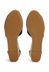 Schwarze Stoffsandalen mit einer strukturierten, naturfarbenen Sohle. Die Sohle weist ein geripptes Muster auf und der Markenname ist auf der Ferse aufgedruckt.