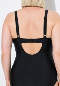 Costume da bagno intero nero con spalline regolabili, chiusura a gancio sul retro e dettaglio con apertura ovale. Tessuto morbido e elasticizzato.