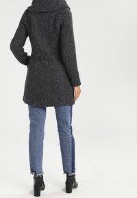 Sorte og hvide teksturerede frakke med bred krave, tætsiddende talje og midt-lår længde, parret med blå jeans og sorte ankelstøvler.