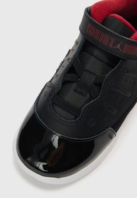 Μαύρο αθλητικό παπούτσι με κομψό σχέδιο, φινίρισμα από δέρμα λάκας, υφή σε διάφορα σημεία και κόκκινο επένδυση στο κολάρο. Περιλαμβάνει κορδόνια και λεπτομέρειες με το λογότυπο.