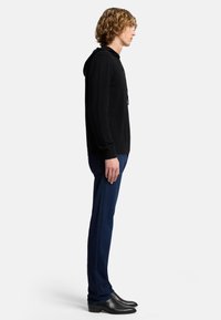Felpa nera con cappuccio e tasca frontale, abbinata a jeans blu e stivali neri alla caviglia. L'abbigliamento presenta un design semplice e lineare con una vestibilità aderente.
