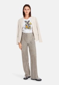 Beiger Blazer über einem weißen T-Shirt mit einem Koala-Graphic, kombiniert mit hellgrauen Wildlederhosen und schwarzen Plateauschuhen.