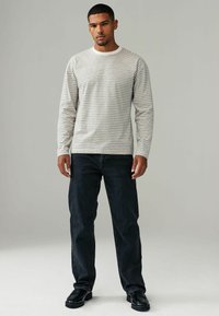 Langærmet stribet skjorte i creme og sort, parret med mørk denim jeans. Skjorten har en rund halsudskæring og en subtil tekstur.