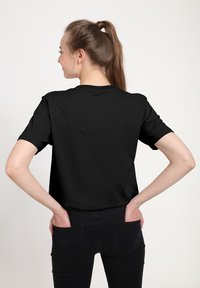 Černé bavlněné tričko s krátkým rukávem, kulatým výstřihem a volným střihem. Materiál vypadá hladce, bez viditelných log nebo vzorů.