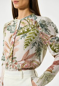 Blusa floreale in tessuto leggero e testurizzato. Presenta vivaci motivi verdi, rosa e beige, maniche lunghe e un collo rotondo.