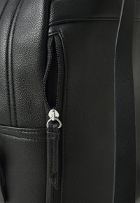 Μαύρη δερμάτινη τσάντα με υφή. Διαθέτει ασημένιο φερμουάρ και θηλιά από ύφασμα, προβάλλοντας έναν κομψό και μοντέρνο σχεδιασμό.