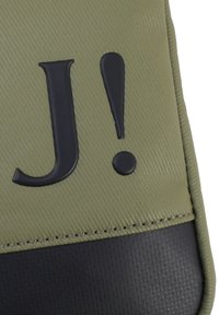 Material texturizzato verde oliva con accenti neri. Presenta una grande lettera nera "J" e un punto esclamativo nero sulla superficie.