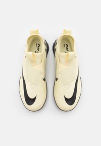 Light yellow athletic shoes with a black Nike swoosh, featuring a smooth synthetic upper, elastic straps, and a textured rubber sole.