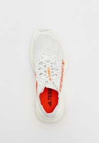 White athletic shoe with mesh upper, orange accents, white sole, and laces. Brand "TERREX" displayed prominently on the sides.