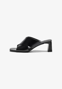 Sandali con tacco in pelle nera, caratterizzati da un design a fascia incrociata, punta quadrata e tacco a blocco. Texture liscia con dettagli essenziali.