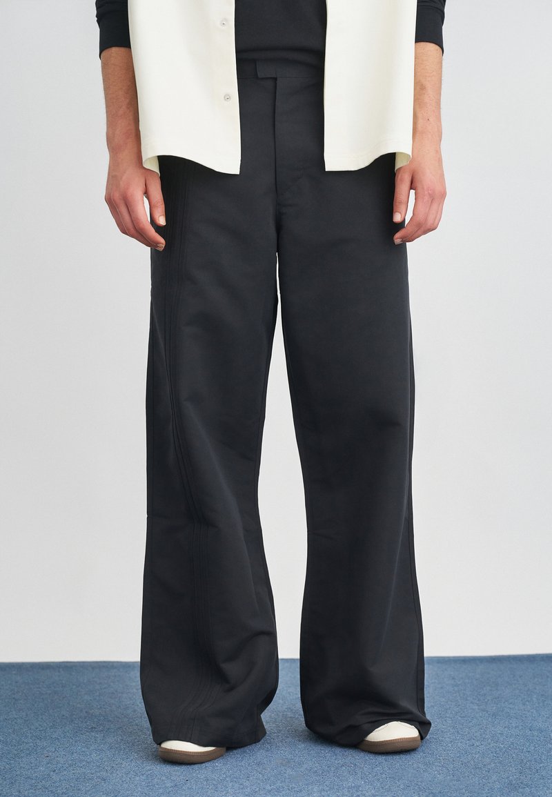 Zwarte wijde broek met een soepele textuur, voorzien van zijdetails in de stiksels en een ontspannen pasvorm, gecombineerd met witte sneakers.