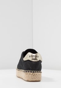 Espadrille en tissu noir avec semelle épaisse en jute tressée et languette dorée embossée du logo "REPLAY", vue de dos.