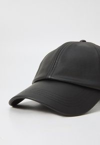 Black leather cap with a curved brim, featuring prominent stitching details and a slightly textured surface, positioned at an angle.