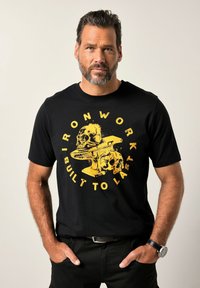 Černé bavlněné tričko s žlutým grafickým designem, na kterém jsou lebky a kovadlina, obklopené textem "KOVÁŘSTVÍ JE STAVĚNO NA DLOUHOU VĚČNOST."