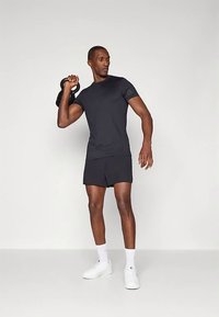 Μαύρο αθλητικό μπλουζάκι και σορτς, με εφαρμοστή σχεδίαση, φορεμένα από ένα άτομο που κρατάει μια αλτήρα kettlebell, σε συνδυασμό με λευκά αθλητικά παπούτσια.