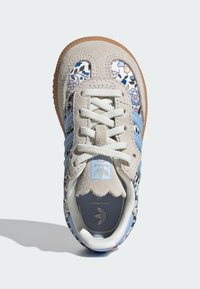 Baskets Adidas beiges et bleu clair avec des motifs floraux, lacets blancs et semelle en gomme, vues de dessus sur un fond blanc.