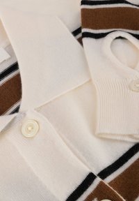 Strikket pikéskjorte i kremfarge med brune og svarte striper. Har krage, korte ermer og knappeåpning. Mykt, teksturert stoff.