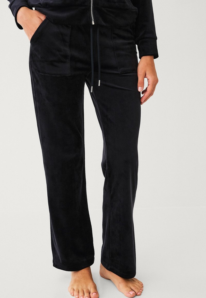 Pantalon de lounge noir velouté avec deux poches frontales, taille avec cordon de serrage ajustable et coupe droite. Texture douce et finition sans coutures.
