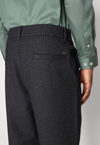 Mörkgrå herringbonebyxor med en strukturerad yta, elastisk midja och ett bakfack med knappstängning.