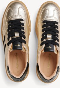 Złote metaliczne sneakersy z czarnymi sznurowadłami, teksturowanymi czarnymi akcentami i beżową podszewką. Posiadają gładkie skórzane wykończenie i kontrastowe paski.