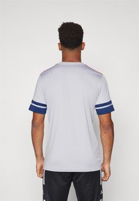 Light gray athletic shirt with navy blue striped sleeves and red accents on the shoulders, made from a smooth, breathable fabric.