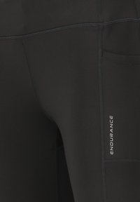 Schwarze Sportleggings aus elastischem Material mit flachen Nähten und einer Seitentasche. Das Wort "ENDURANCE" ist am unteren Rand aufgedruckt.