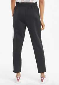 Pantalones de chándal negros con cintura elástica, piernas ajustadas y bolsillos laterales. Hechos de material suave, el diseño presenta un estilo limpio y minimalista.