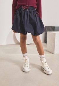 Navy blue, puffed skirt with an elastic waistband and red drawstring; worn with white high-top sneakers and crew-length socks.