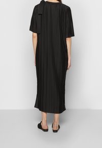 Schwarzes knielanges Kleid mit vertikalen Falten, kurzen Ärmeln und lockerem Sitz. Verfügt über eine Schleifendetail am Schulterbereich und einen geraden Saum.