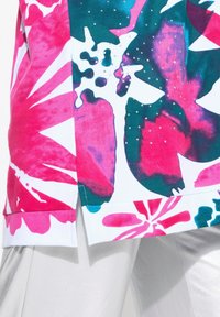 Halenka s květinovým vzorem v živých odstínech růžové, tyrkysové a bílé. Má hladkou texturu s dekorativními flitry a detail vrstveného lemu.