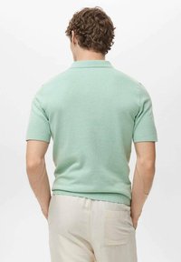 Polo shirt verde menta a maniche corte con tessuto a maglia testurizzato, design aderente e colletto a coste, indossato con pantaloni in lino color crema.