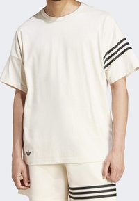 Krämfärgad t-shirt med korta ärmar i mjuk bomull, med svarta ränder på ärmarna och en liten svart logotyp vid fållen.