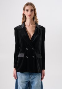 Zwarte fluwelen dubbelgeknoopt colbert met satijnen revers, voorzien van twee voorzakken en grote knopen, gedragen over losse blauwe denim.