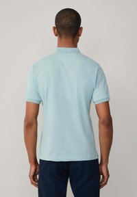 Světle modrá polo košile vyrobená z hladké tkaniny, s klasickým límcem a krátkými rukávy. Pevný lem s bočními rozparky pro větší pohodlí.