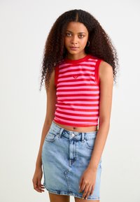Top corto a righe rosse e rosa con design senza maniche, texture a costine e piccolo logo decorativo. Abbinato a una mini gonna di jeans blu chiaro.