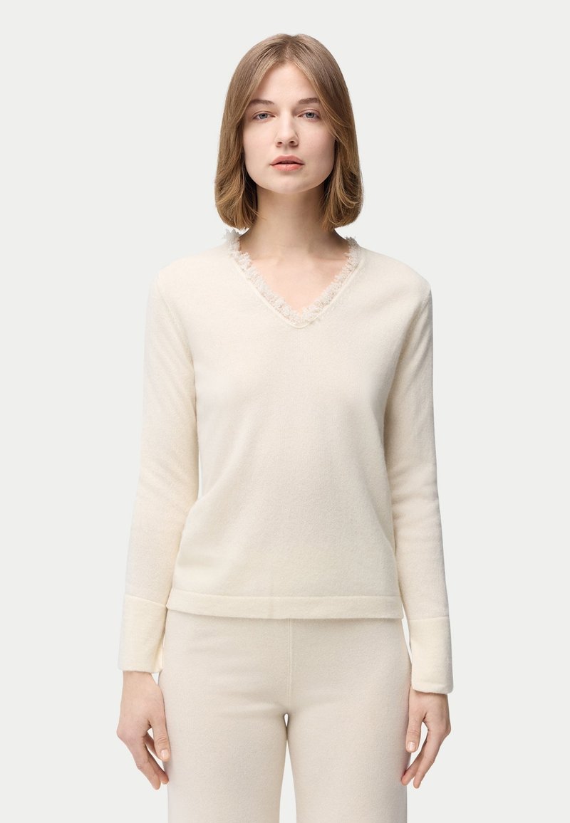 Cremefarbener Pullover mit V-Ausschnitt und Rüschenbesatz, aus weichem Stoff gefertigt. Lange Ärmel und gerader Saum sorgen für eine entspannte Passform.