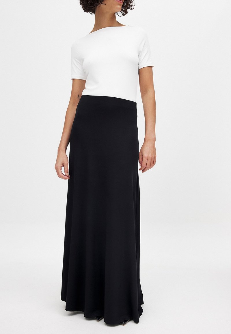 Zwarte maxirok met een soepele, vloeiende uitstraling en een hoge tailleband, gecombineerd met een aansluitend wit T-shirt met korte mouwen. Minimalistische stijl.