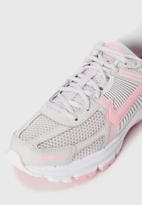 Basket de course Nike blanche et rose avec une tige en mesh, couture détaillée et lacets, présentée dans une vue avant en gros plan et en angle.